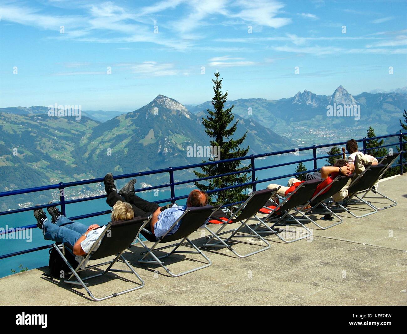 A group of tourists enjoy a scenic view of the Swiss Alps while lounging on an observation deck in Beckenried, Switzerland. Stock Photo