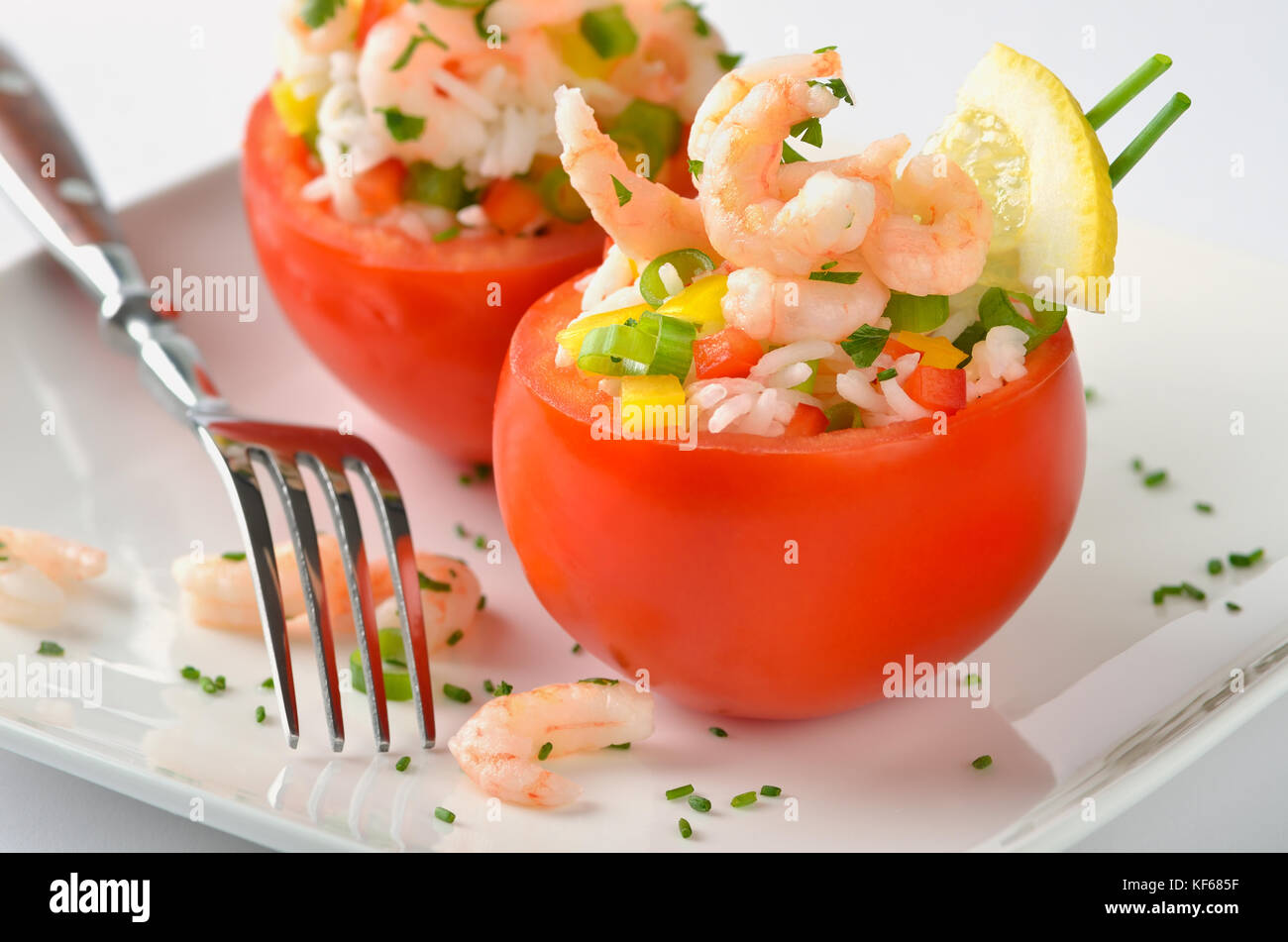 Stuffed, fresh tomatoes with shrimps, rice, bell peppers, spring onions, lemon, chives and parsley Stock Photo