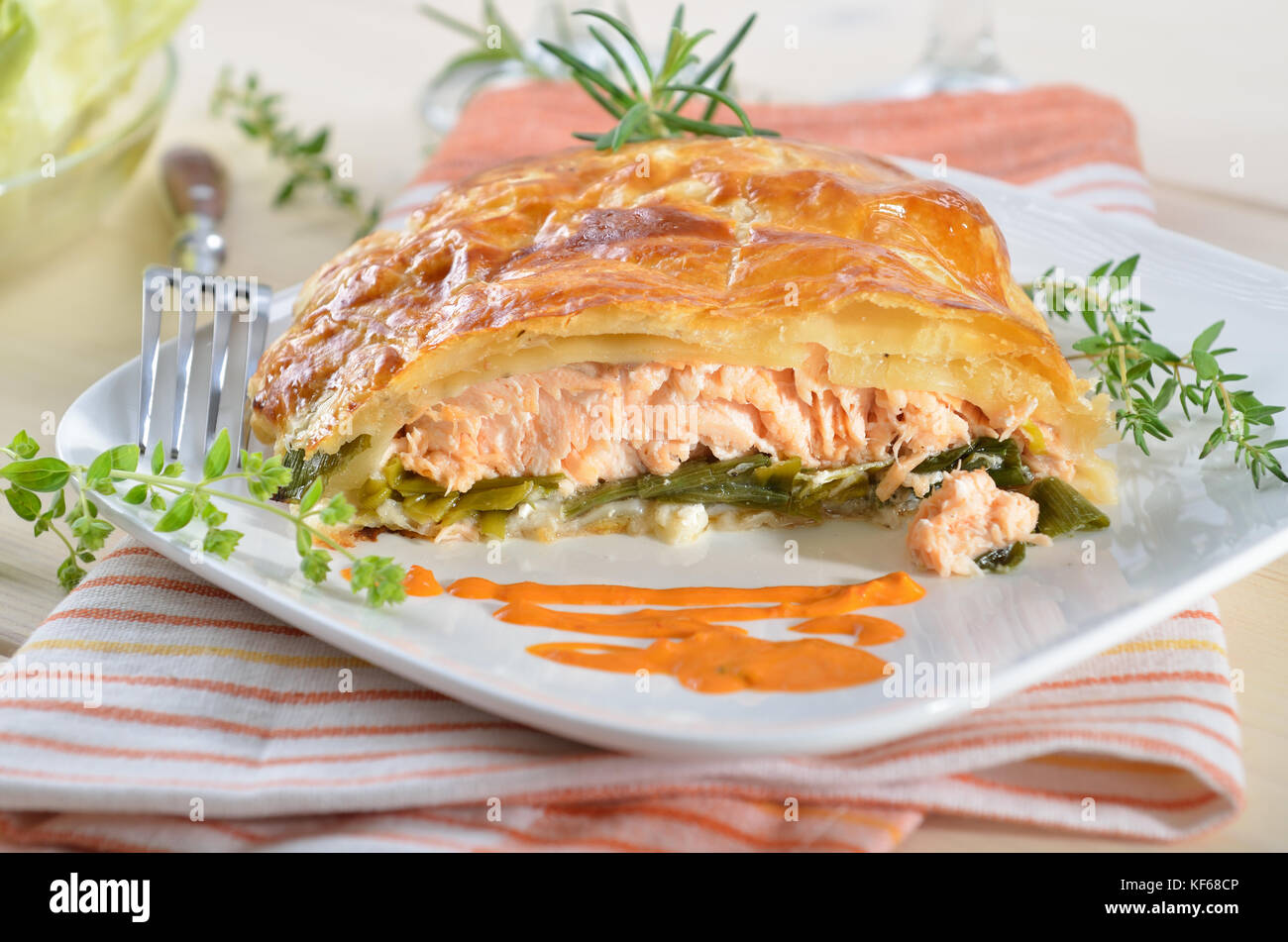Salmon fillet on leek, baked in puff pastry, served with herbs, sauce and side salad Stock Photo