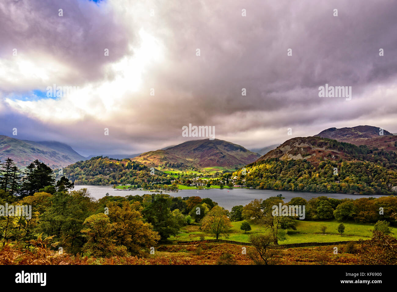 Looking across Ullswater to the sunlit village of Glenridding with the fells behind Stock Photo