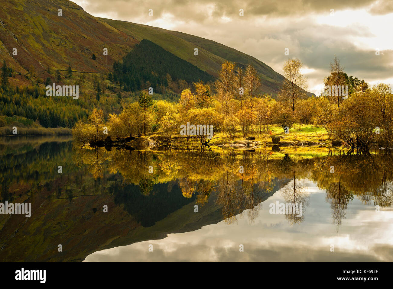 Golden sunlit symmetrical autumn reflections on Thirlmere, Lake District National Park Stock Photo