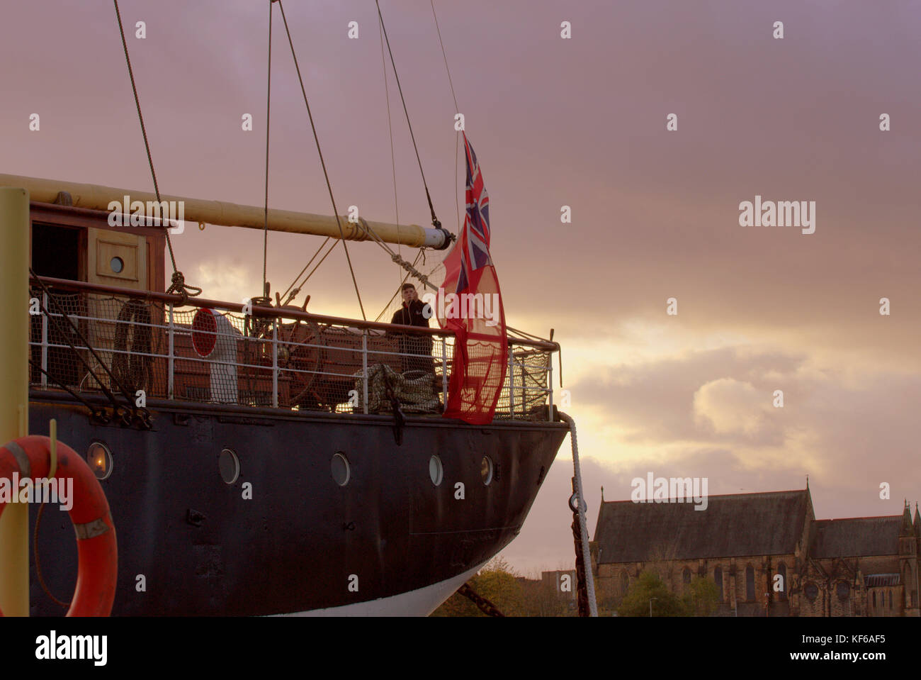 young boy lowering british marine flag on the ship glenlee at the riverside museum glasgow scotland sunset Stock Photo