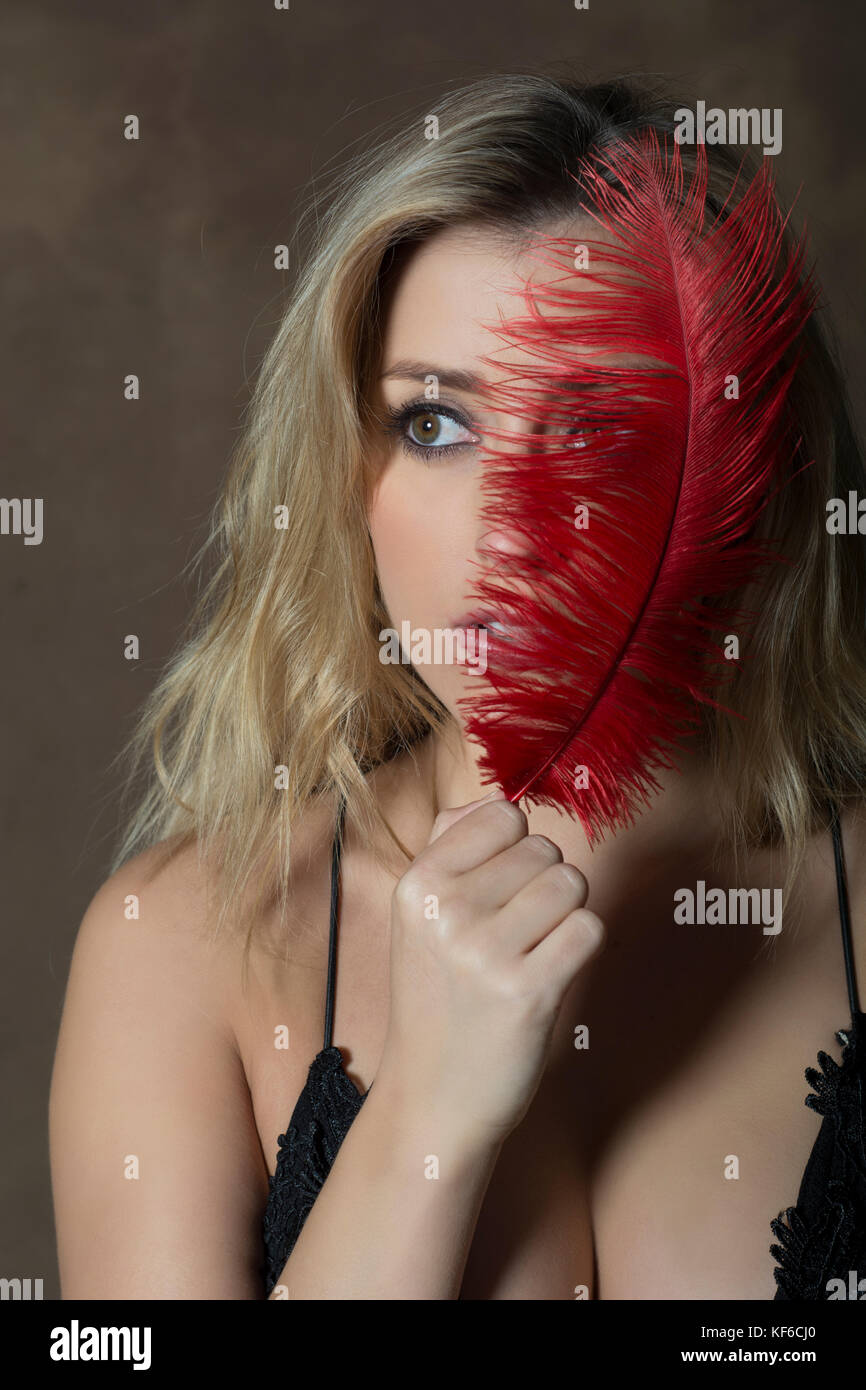 Beautiful young woman hiding face with a red feather Stock Photo - Alamy