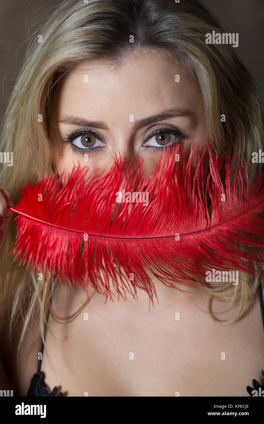 Beautiful young woman hiding face with a red feather Stock Photo - Alamy