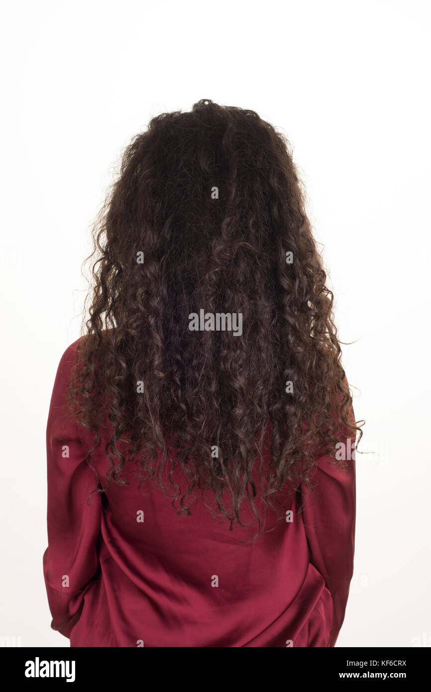Rear view of a young woman with long curly dark hair standing against a ...