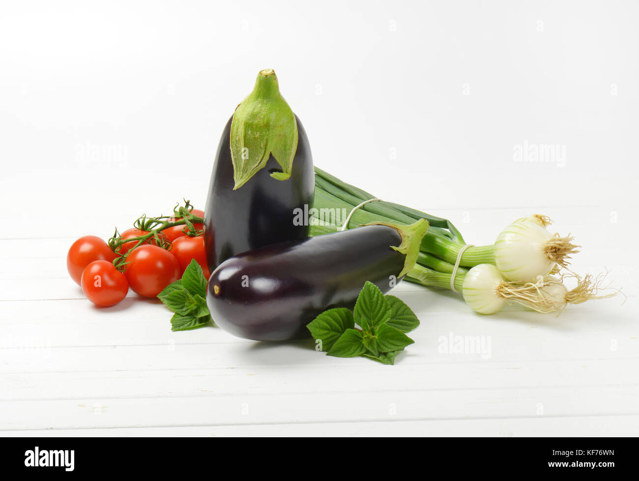 fresh eggplants, tomatoes and spring onion on white wooden background