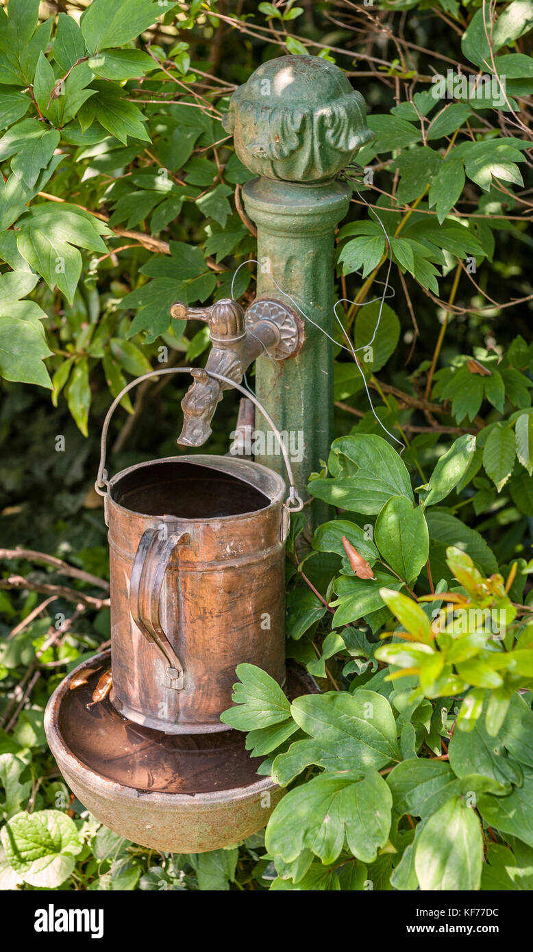 Italy. An antique copper watering can hangs from a tap in the shape of an animal head, in a corner of an Italian garden Stock Photo
