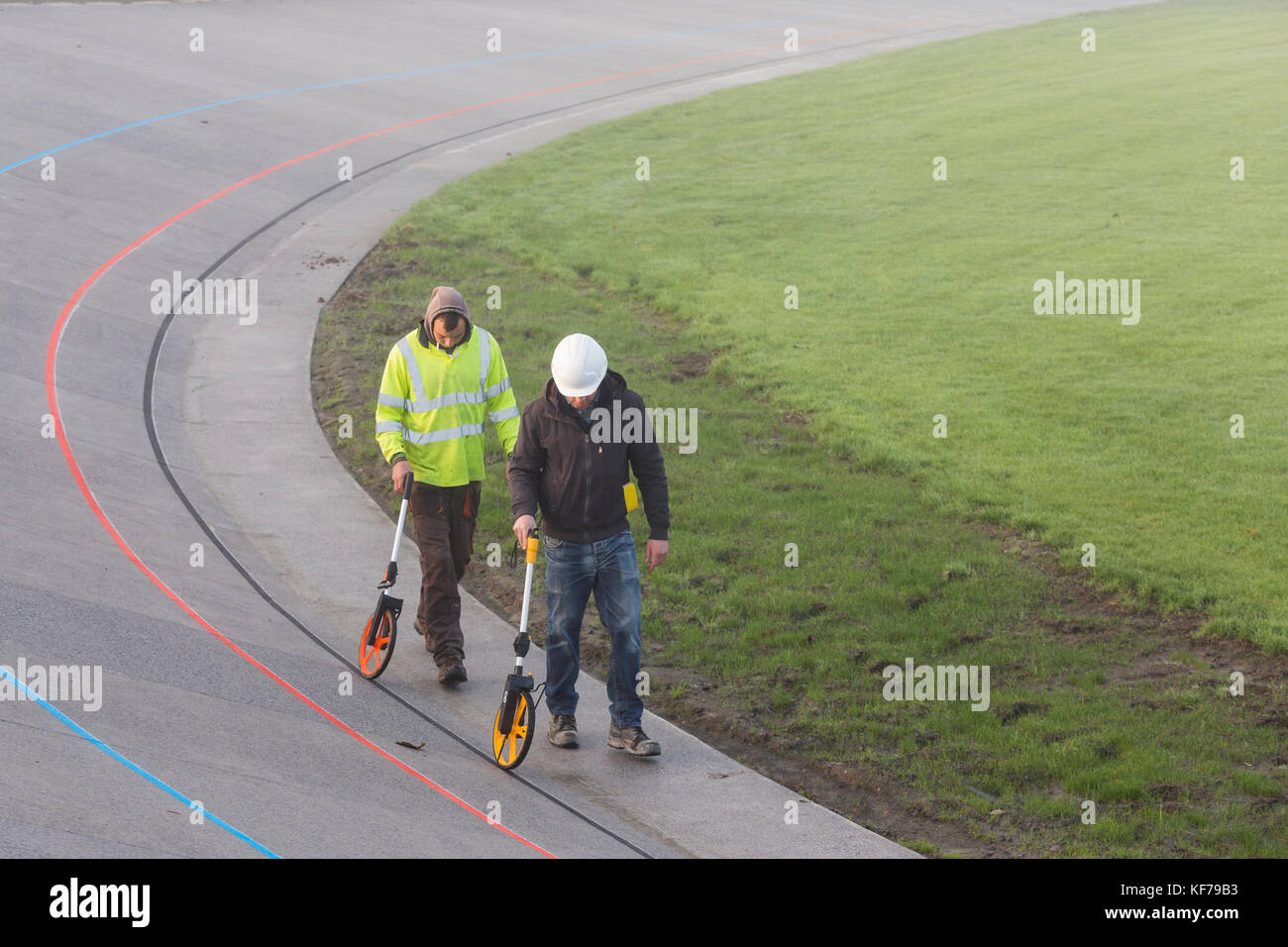 Two men using trundle wheels measure the distance around the velodrome