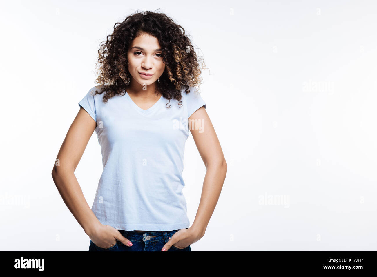 Curly young woman posing with her hands in pockets Stock Photo - Alamy