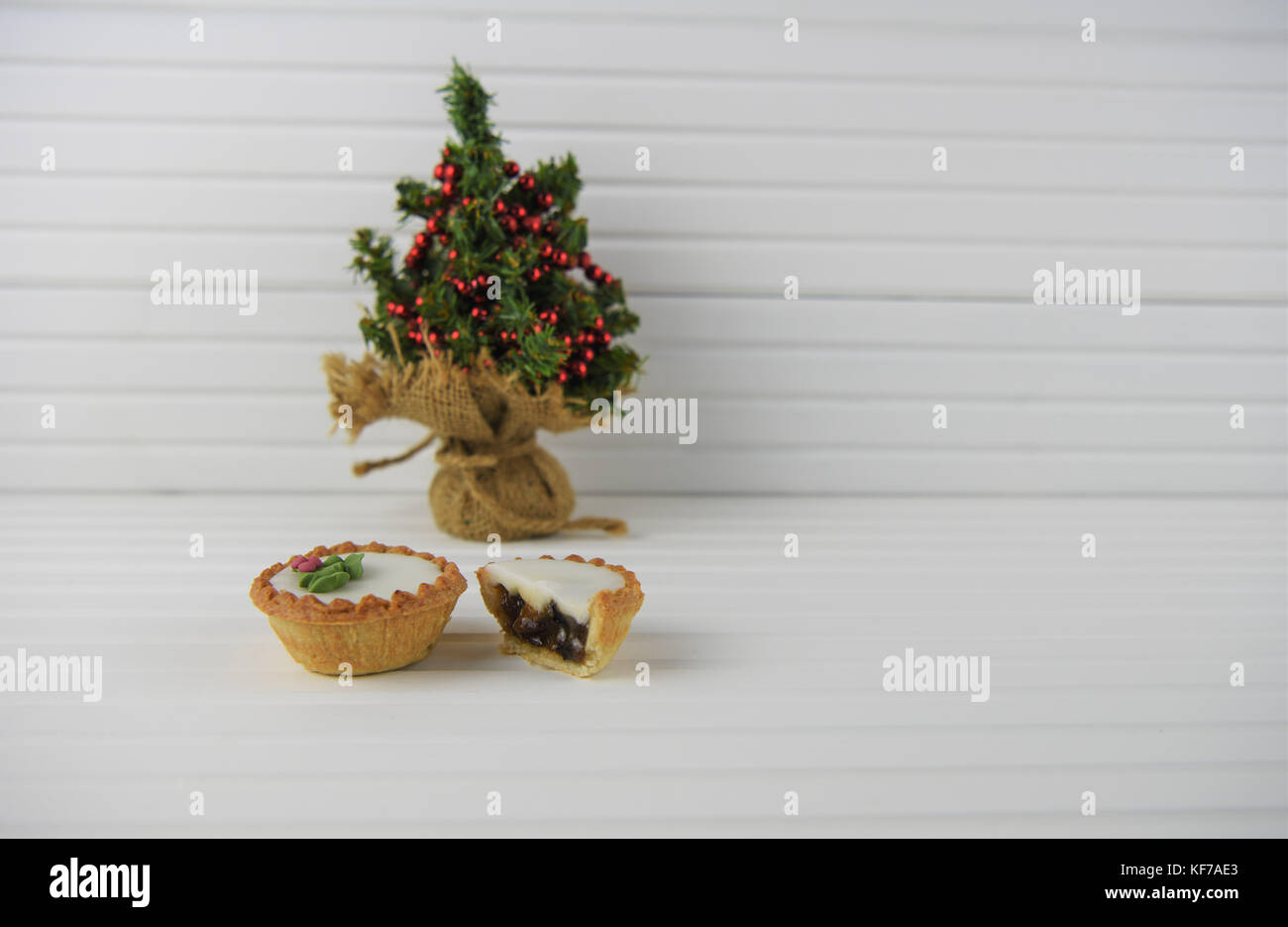 tasty Christmas food photography image of iced mince pies pie and ornament green xmas tree and beads with bright white wood background Stock Photo