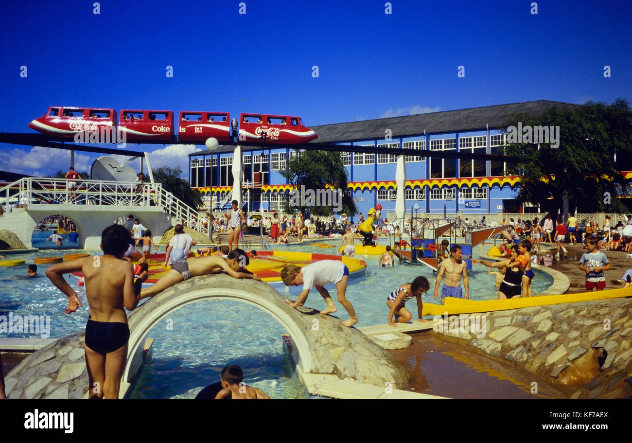 A monorail passing over the sun splash outdoor swimming pool at Butlins Minehead. Formally Somerwest World, England, UK, Circa 1980's Stock Photo