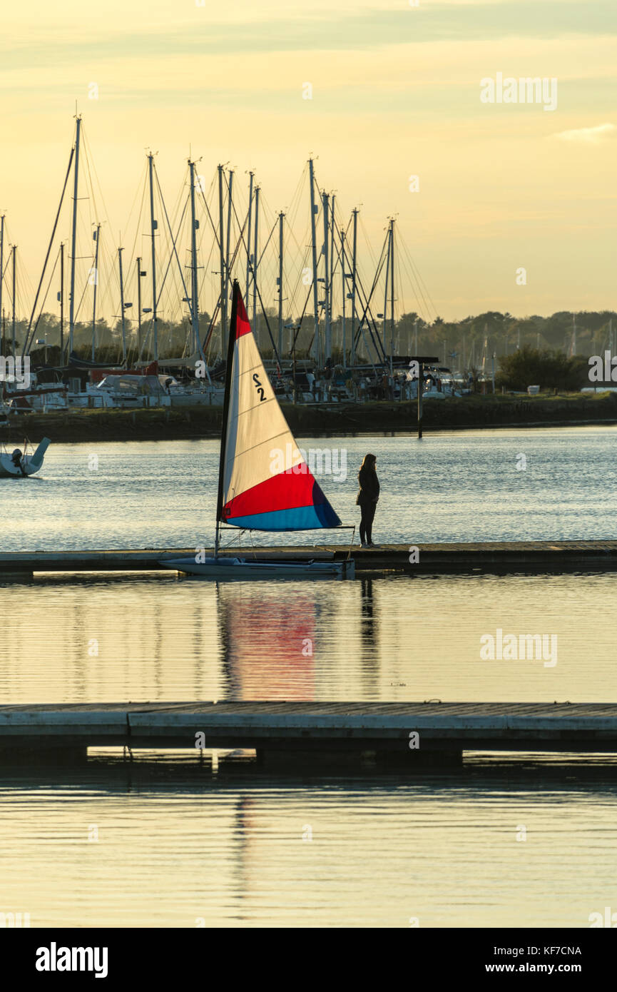 small sailing dinghy with white, red and blue sail, moored on a pontoon