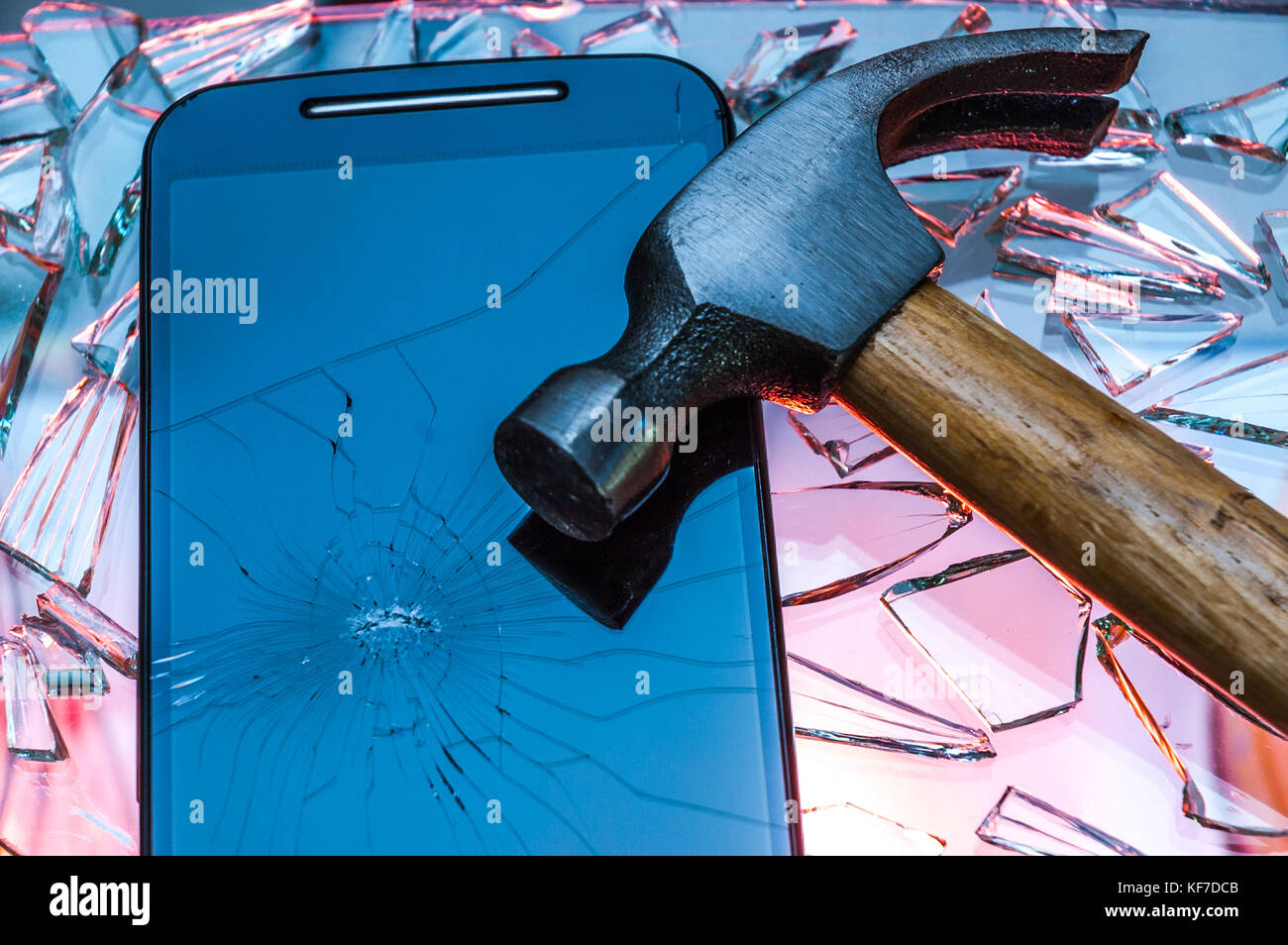 Broken black smartphone with cracked screen lying on smashed broken glass with hammer on top of it Stock Photo