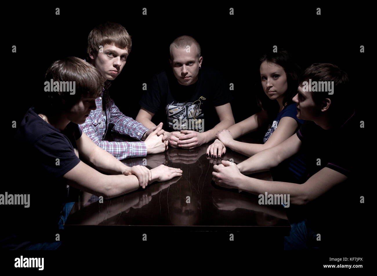 The company of young people sitting at a table in a dark room.Indoor