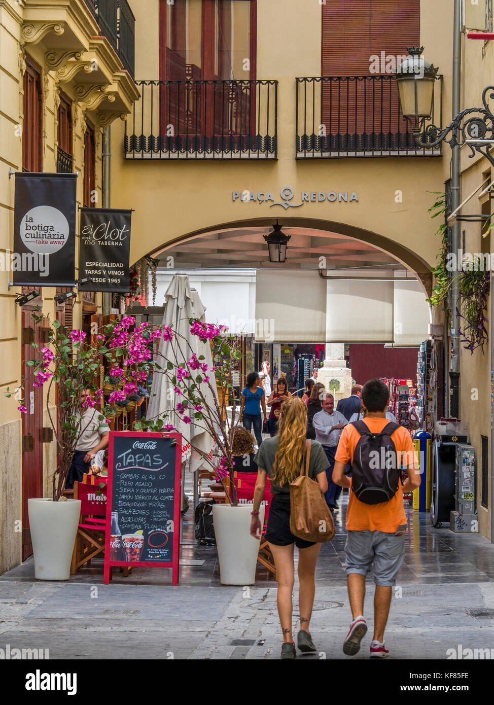 Two people walking towards Plaça Redona, a circular pedestrianised area containing boutique stalls, shops and tapas bars, Valencia, Spain Stock Photo