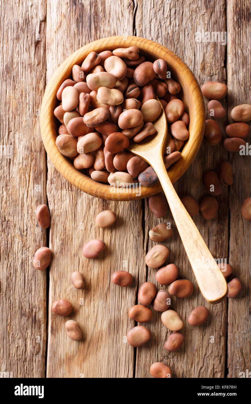 Dried broad beans close-up in a wooden bowl on the table. Vertical top view from above Stock Photo