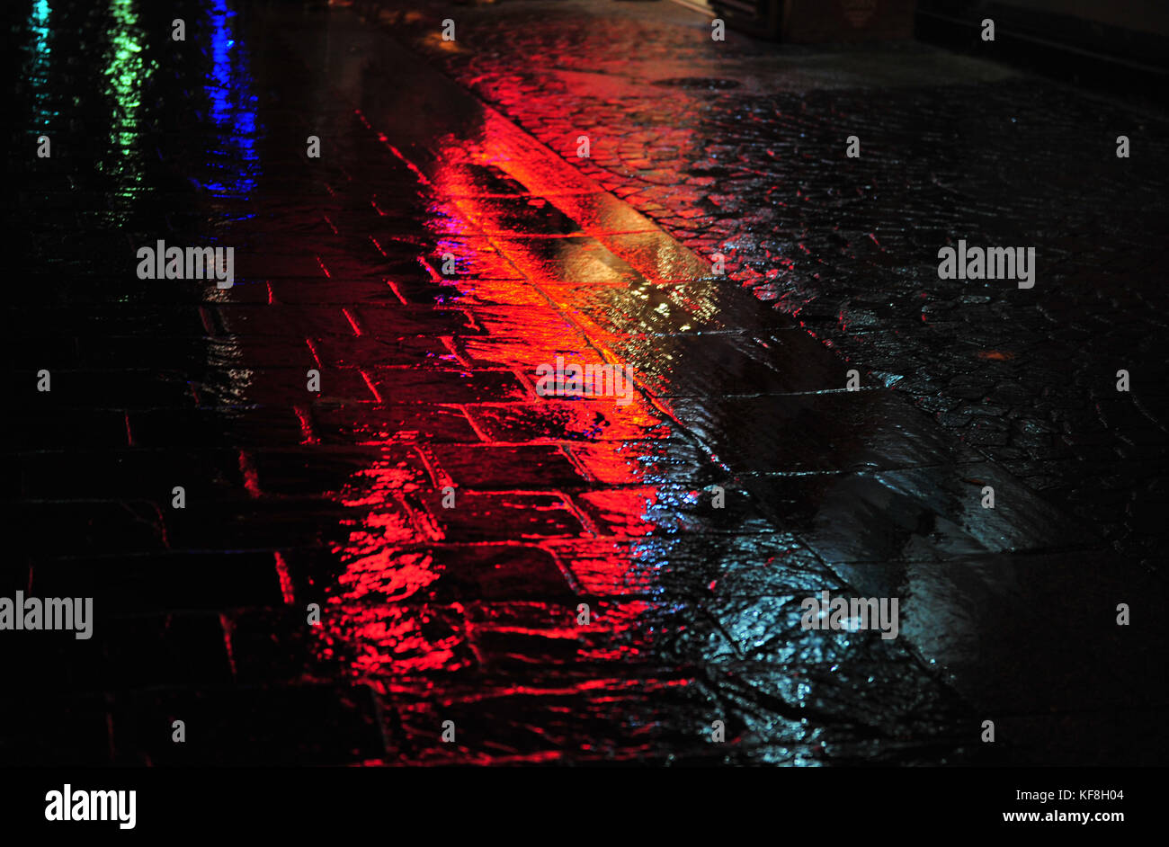 Colorful reflections on wet dark cobblestone street.  Rainy evening. Horizontal photo with copy space. Stock Photo