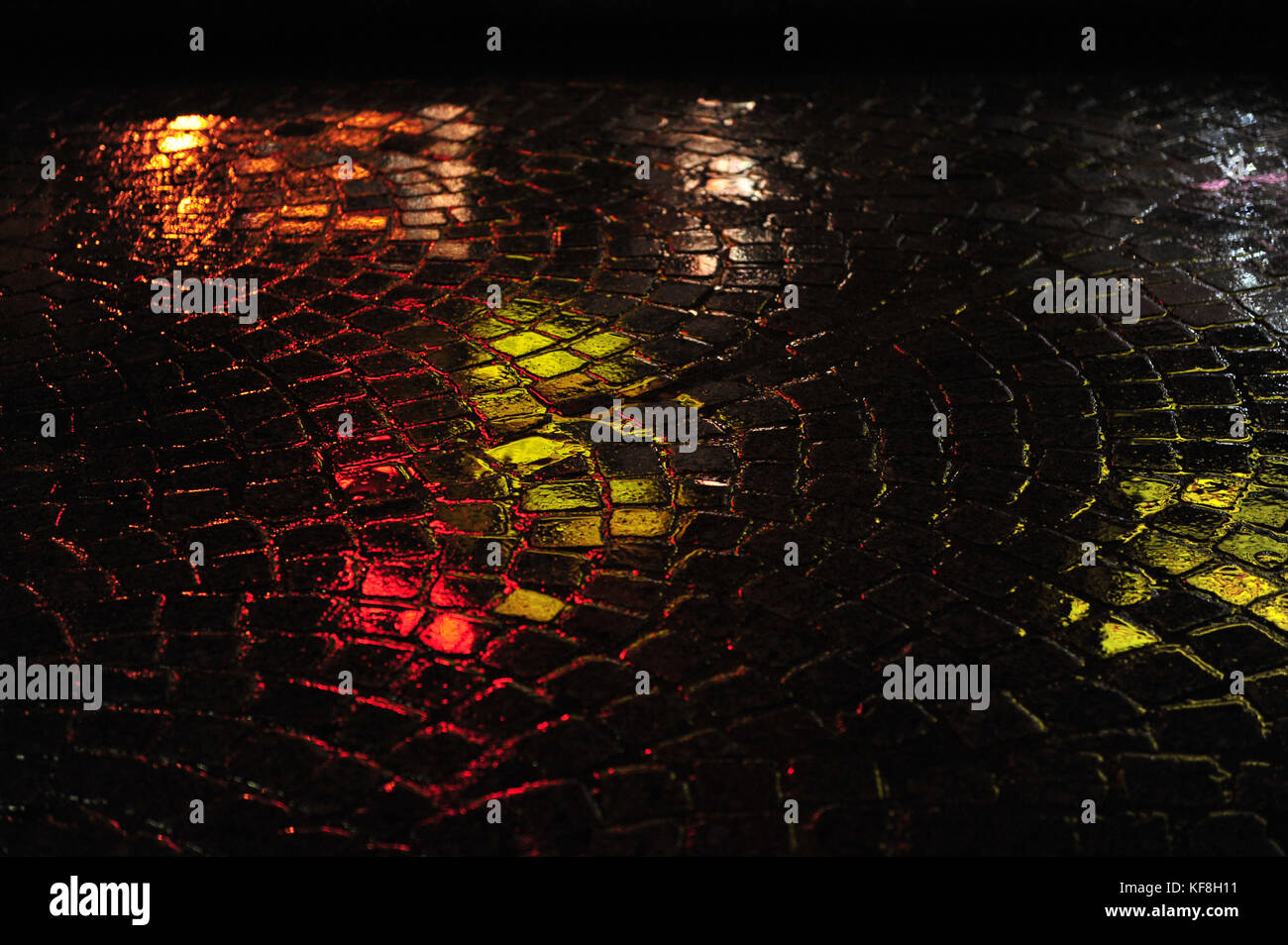 Reflections in green and red on wet, rainy street of cobblestone.  Closeup horizontal photo at night. Evening shot in the dark. Stock Photo