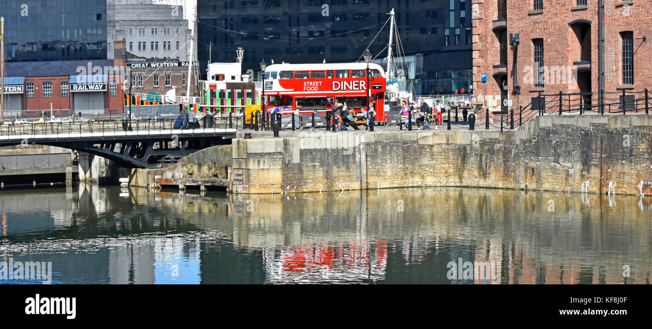 Reflections in Liverpool Albert Dock of red Routemaster bus converted into cafe diner come restaurant facility in busy tourism area in Merseyside UK Stock Photo