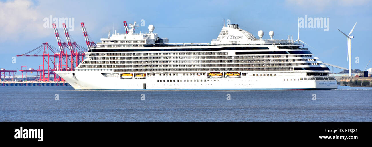 Regent Seven Seas Explorer cruise ship liner passing red cranes & wind turbines of Seaforth Docks after departing Liverpool waterfront cruise terminal Stock Photo