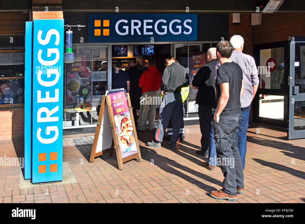 Men mostly lorry truck transport driver queuing to enter Greggs food & bakery shop at Lymm M6 motorway services in Cheshire England UK Stock Photo