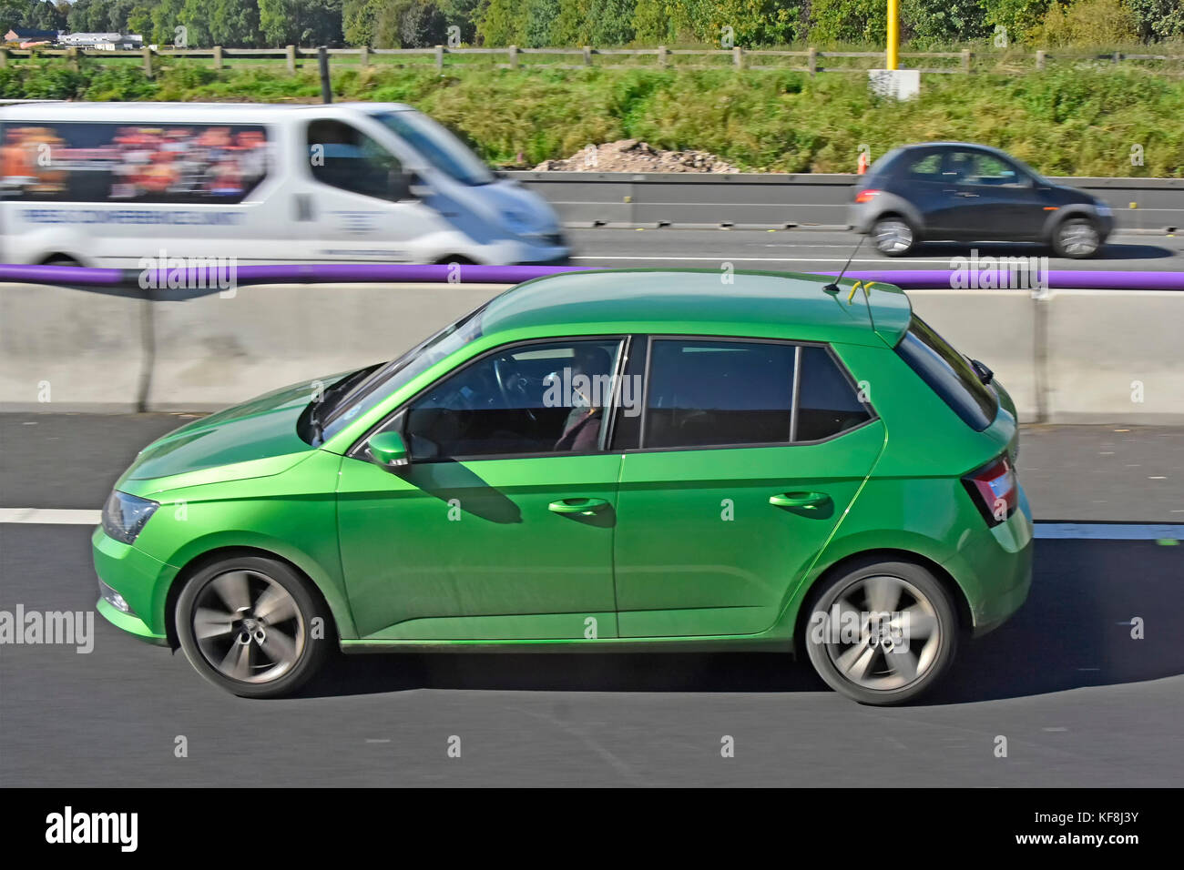 Green hatchback car driving along lane three of UK motorway with  temporary sectional concrete crash barrier during road works  woman passenger in car Stock Photo