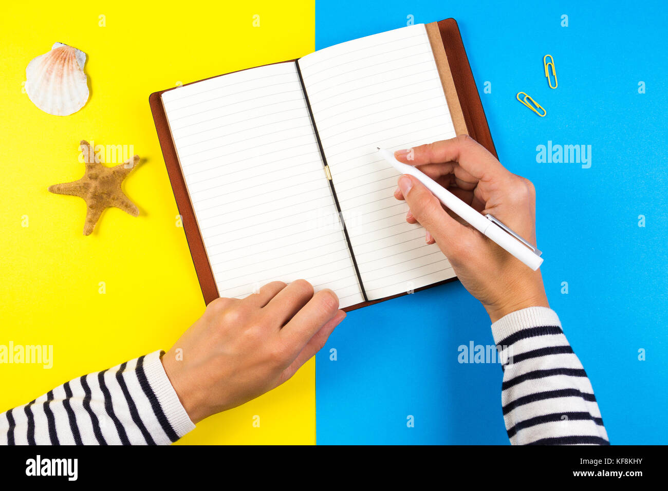 Woman hand writing in notebook over blue and yellow background Stock Photo