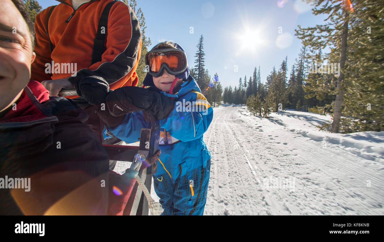 USA, Oregon, Bend, a young boy stands with the musher on the footboards while being pulled around Mt. Bachelor by the sled dogs Stock Photo