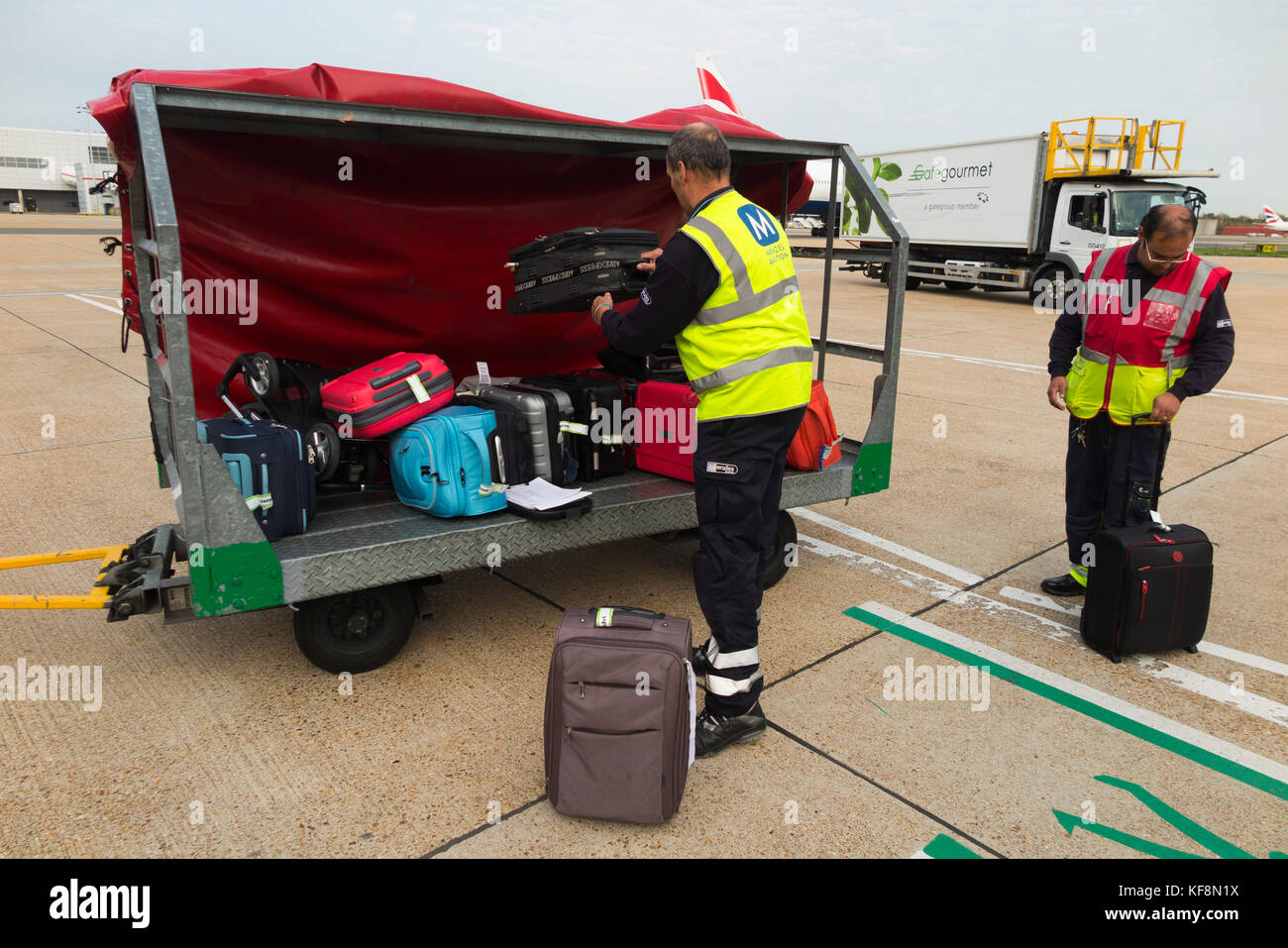 Baggage handlers trolley / truck carrier / vehicle / aircraft loader / container / ground support staff / carrying & loading passenger hold luggage. Stock Photo