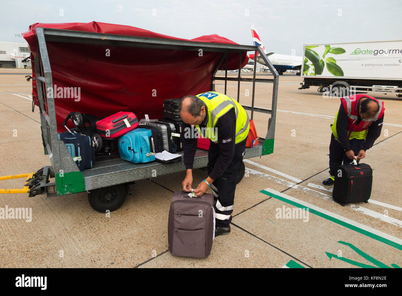Baggage handlers trolley / truck carrier / vehicle / aircraft loader / container / ground support staff / carrying & loading passenger hold luggage. Stock Photo