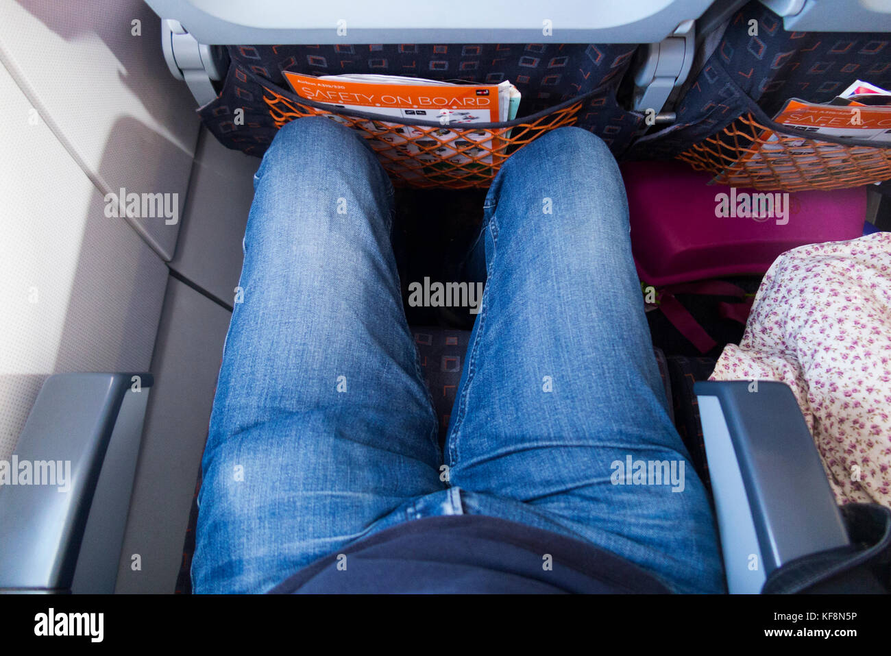 Passenger sitting in seat on an airplane / aeroplane / plane showing passengers legs and knees in a restricted space, on an Easyjet Airbus A320-214 Stock Photo