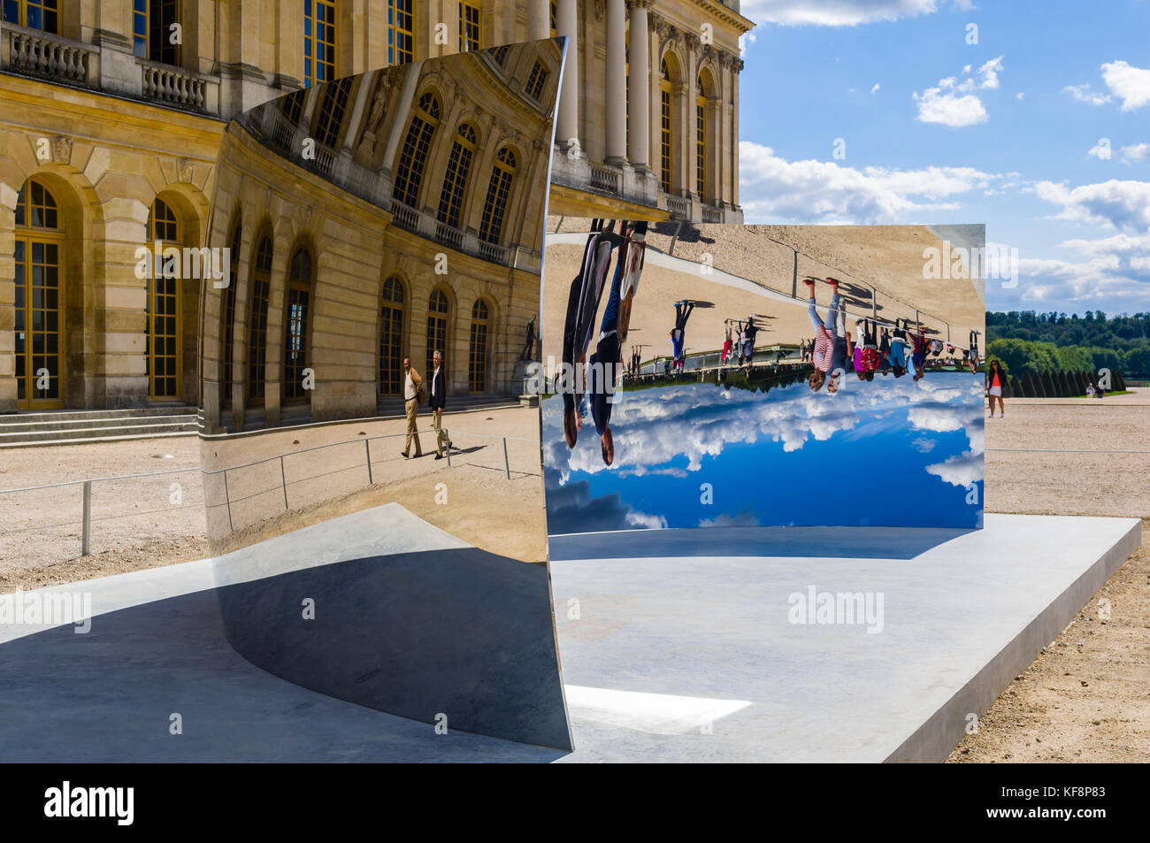 Art installation in the gardens of Chateau de Versailles in 2015.  The artwork, called 'C-Curve' by British contemporary artist, Anish Kapoor, is pictured in front of the Chateau, against a blue cloudy sky, reflecting the sky, with visitors reflected. Stock Photo