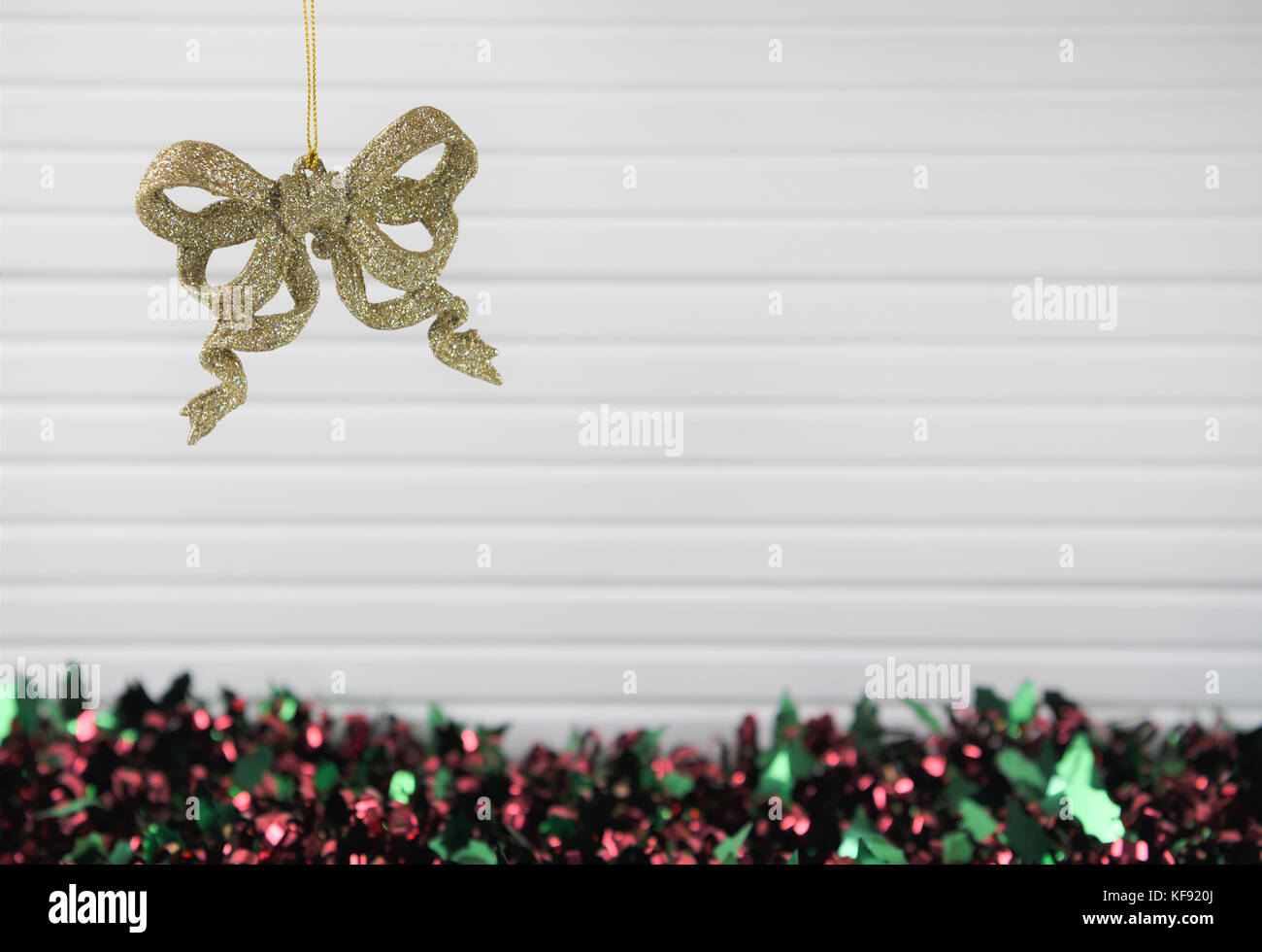 Christmas photography picture of xmas tree decoration hanging up of gold glitter sparkle bows with colored red green tinsel and white wood background Stock Photo