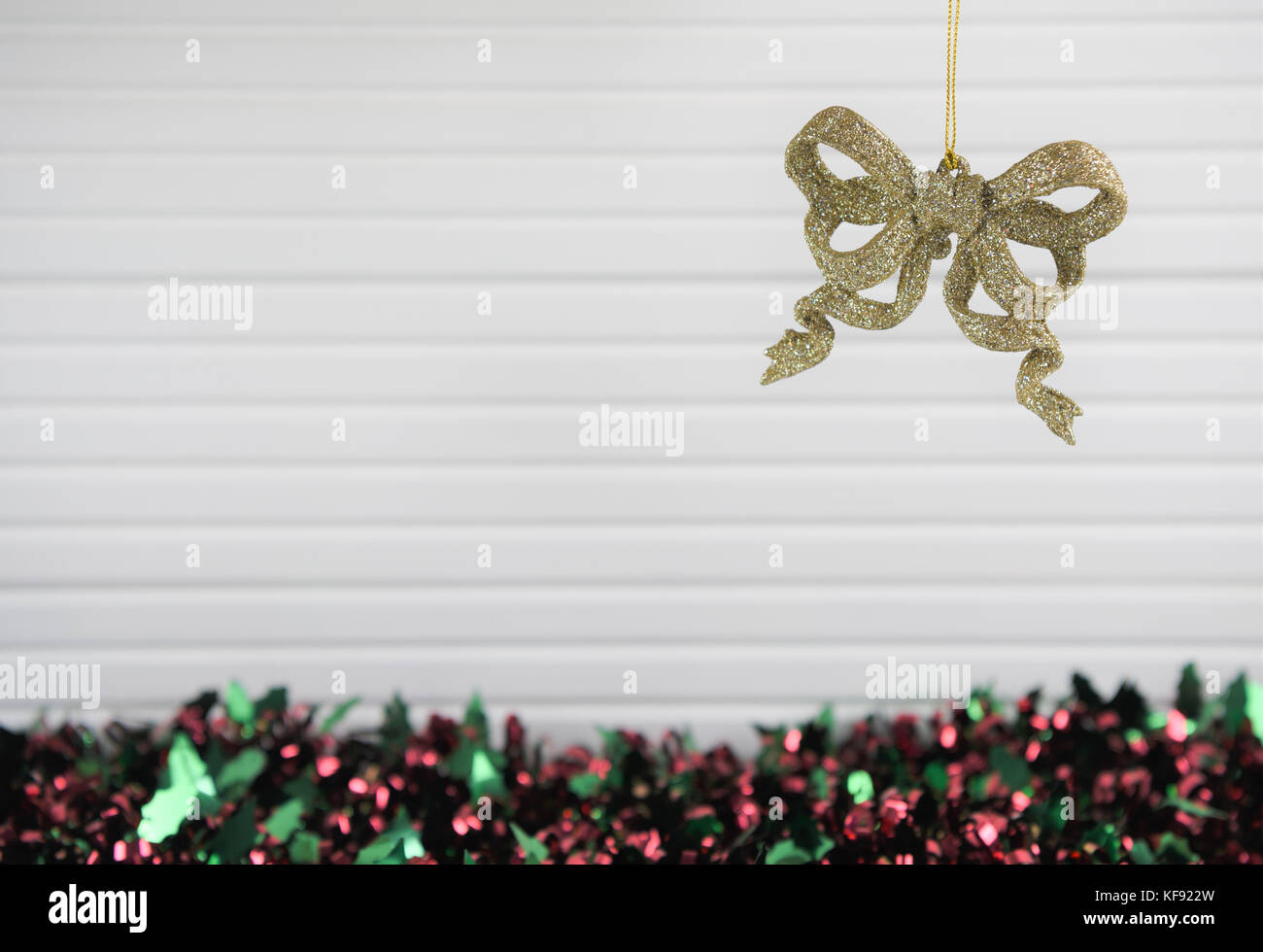 Christmas photography picture of xmas tree decoration hanging up of gold glitter sparkle bows with colored red green tinsel and white wood background Stock Photo