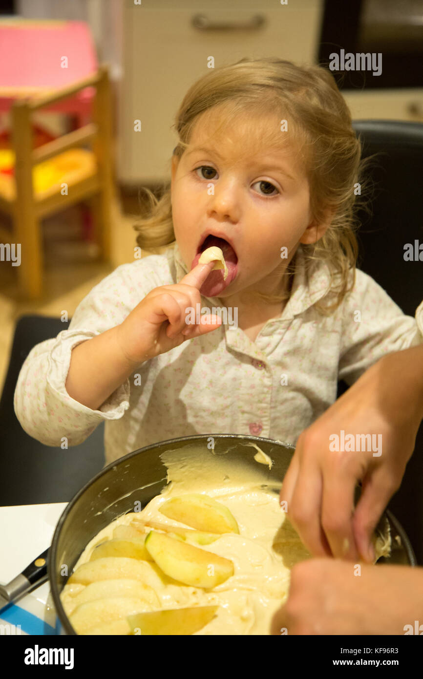 A young toddler girl licking the mixture prepared for a cake. She is almost 2 years old Stock Photo