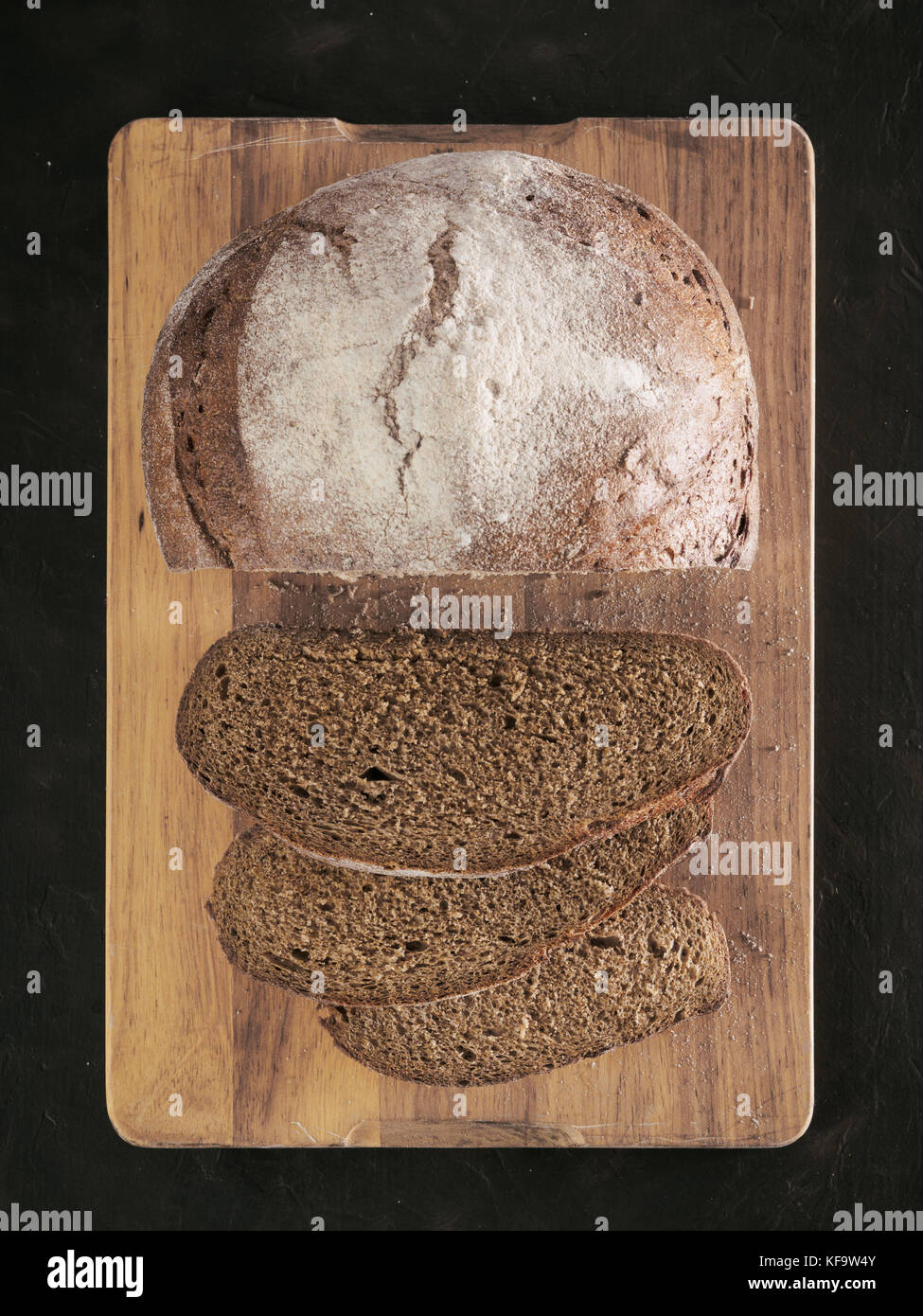 Sliced homemade sourdough rye bread on cutting board over black textured background with rye flour. Top view or flat-lay. Low key Stock Photo