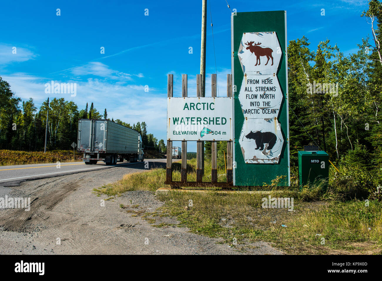 ARCTIC WATERSHED, ONTARIO, CANAD: trucks passing a signpost on Transcanada Highway 101 indicating the watershed between hudsonbay and arctic ocean bet Stock Photo