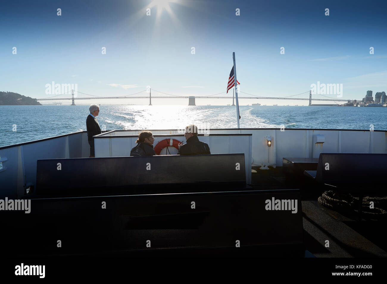 Looking Aft Towards The San Francisco-Oakland Bay Bridge From The Deck Of A Blue And Gold Fleet Ferry, Passengers Enjoying The Fine Weather And View. Stock Photo