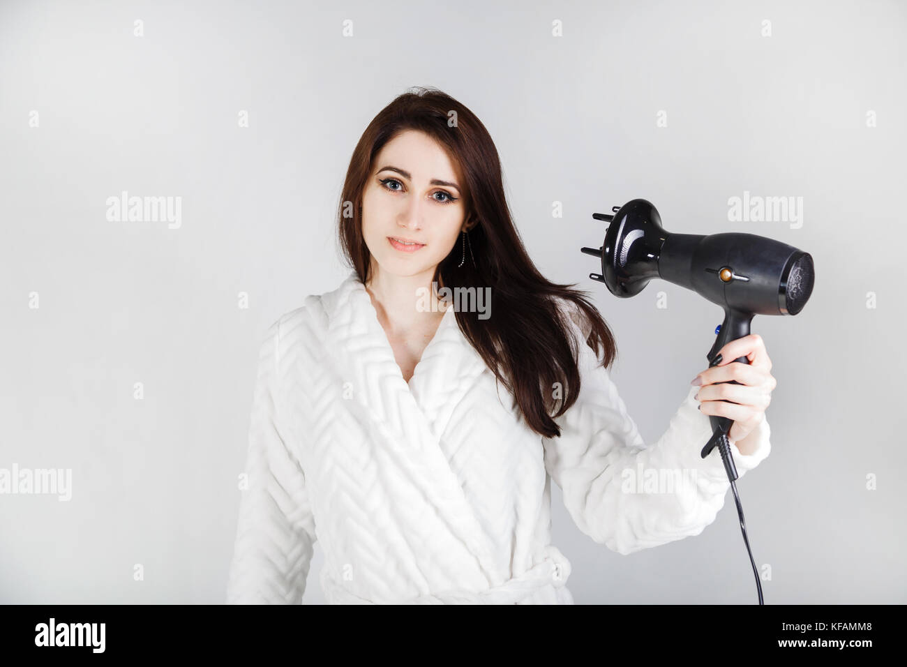 girl in a bathrobe with a hair dryer dries her hair against a