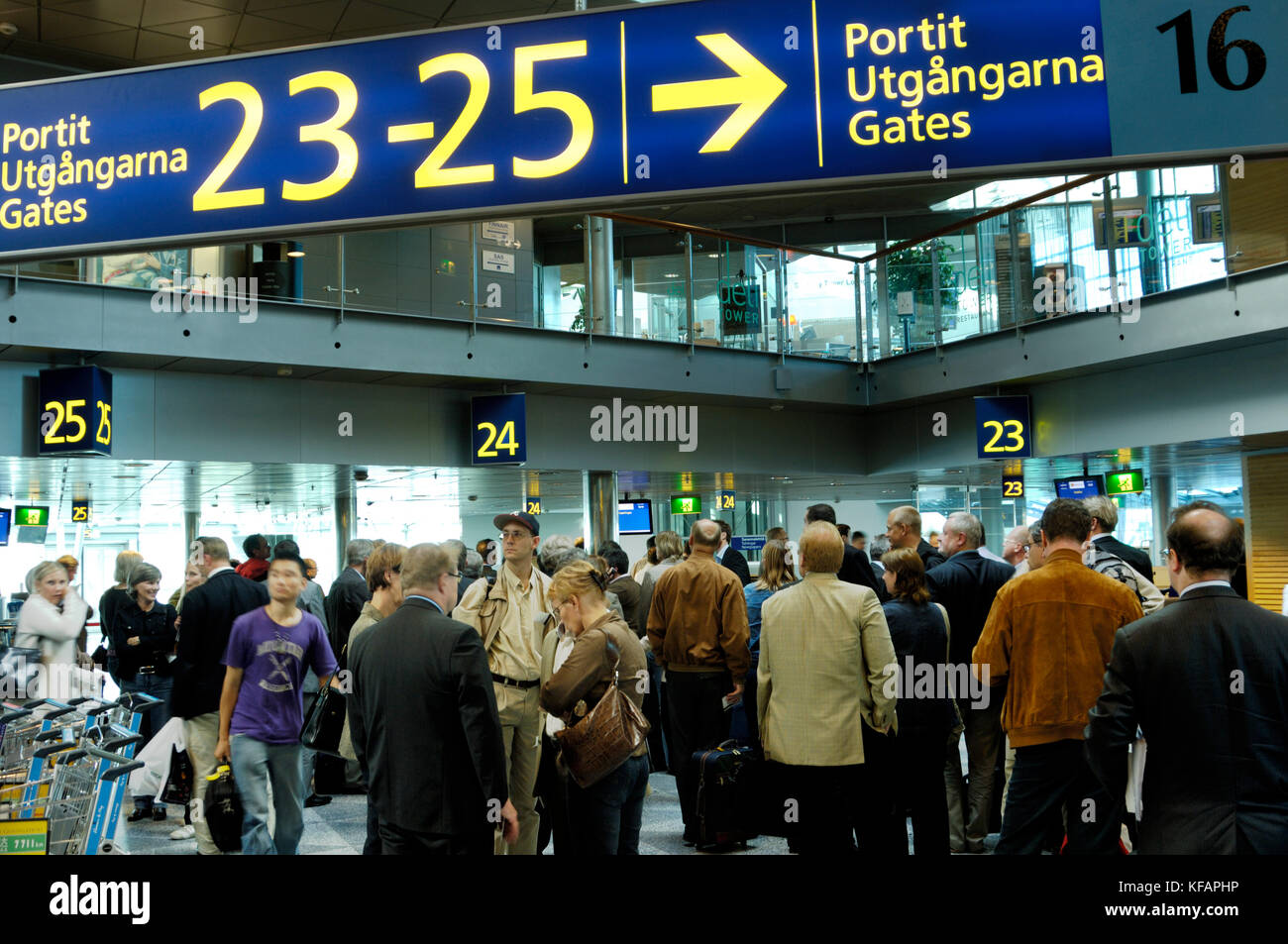 passengers with bags under sign for Gates 23 to 25 in Finnish, Swedish and English languages in the terminal Stock Photo