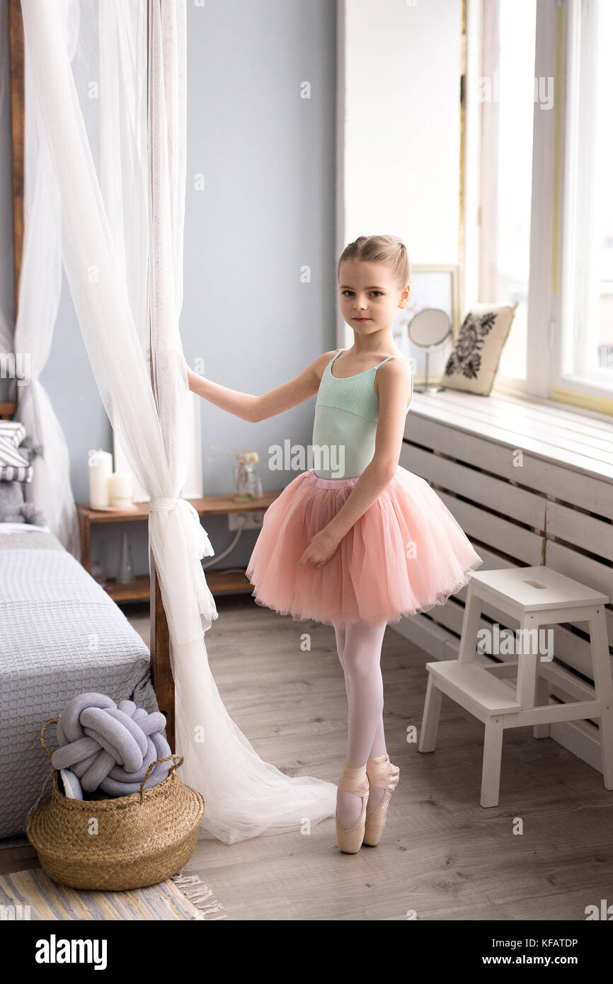 Cute little ballerina in pink ballet costume and pointe shoes is dancing in the room. Child girl is studying ballet. Stock Photo