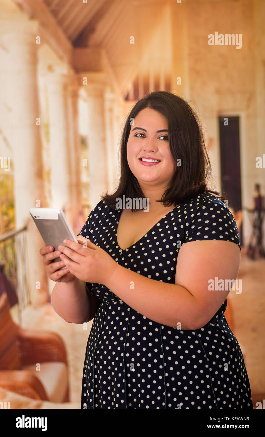 Close up of beautiful fat woman in a beautiful dress using her tablet in a blurred background Stock Photo