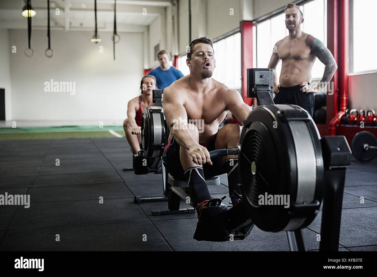 Man Exercising On Rowing Machine While Instructor Looking At Him Stock ...