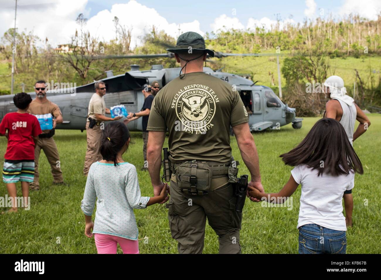 A U.S. Department of Homeland Security officer escorts two Puerto Rican children to a U.S. Navy MH-60S Seahawk helicopter for emergency supplies during relief efforts in the aftermath of Hurricane Maria October 14, 2017 in San Salvador, Puerto Rico.   (photo by Jacob Andrew Goff via Planetpix) Stock Photo