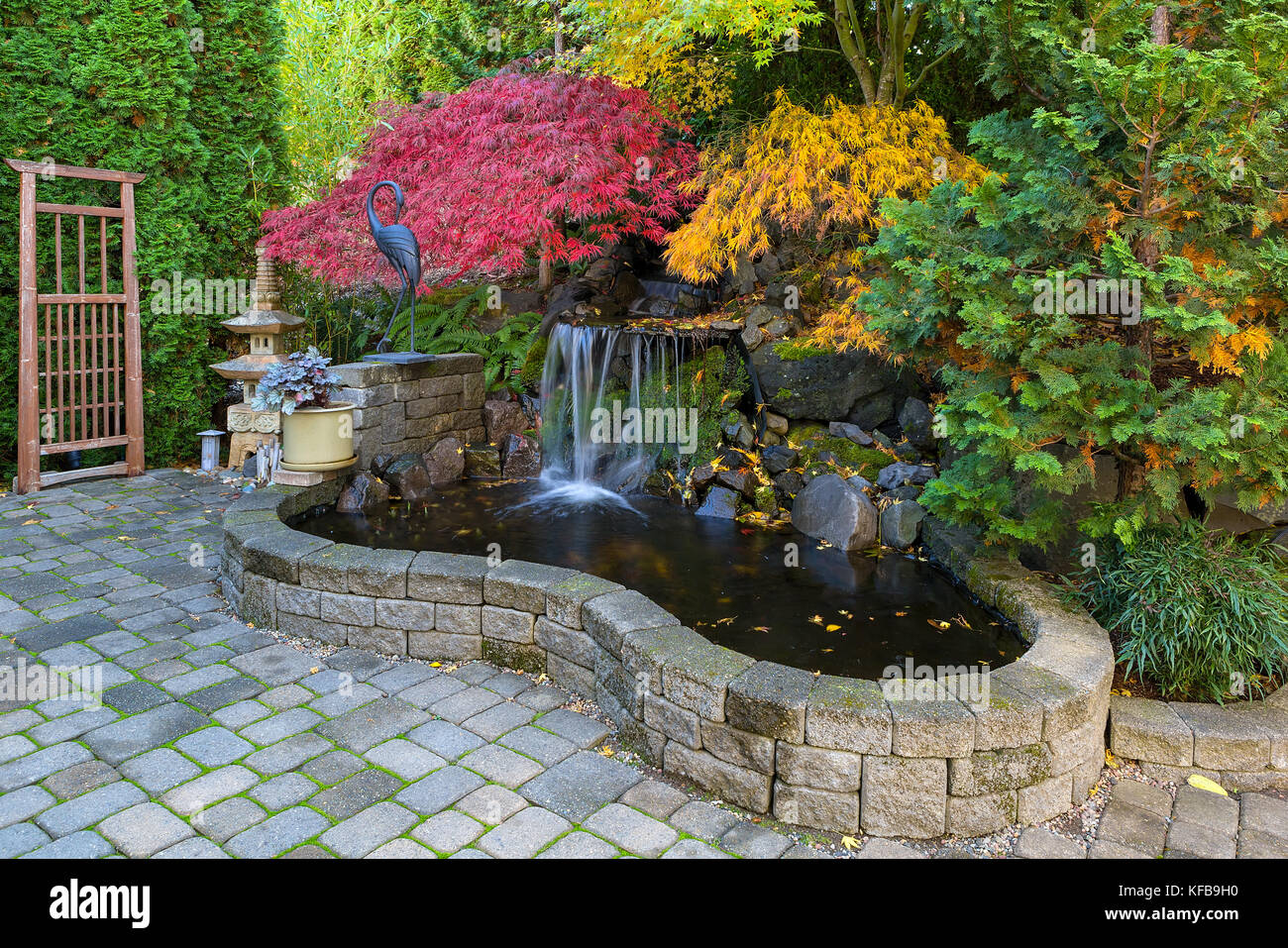 Home garden waterfall pond with brick paver stone hardscape and trees in fall season colors Stock Photo