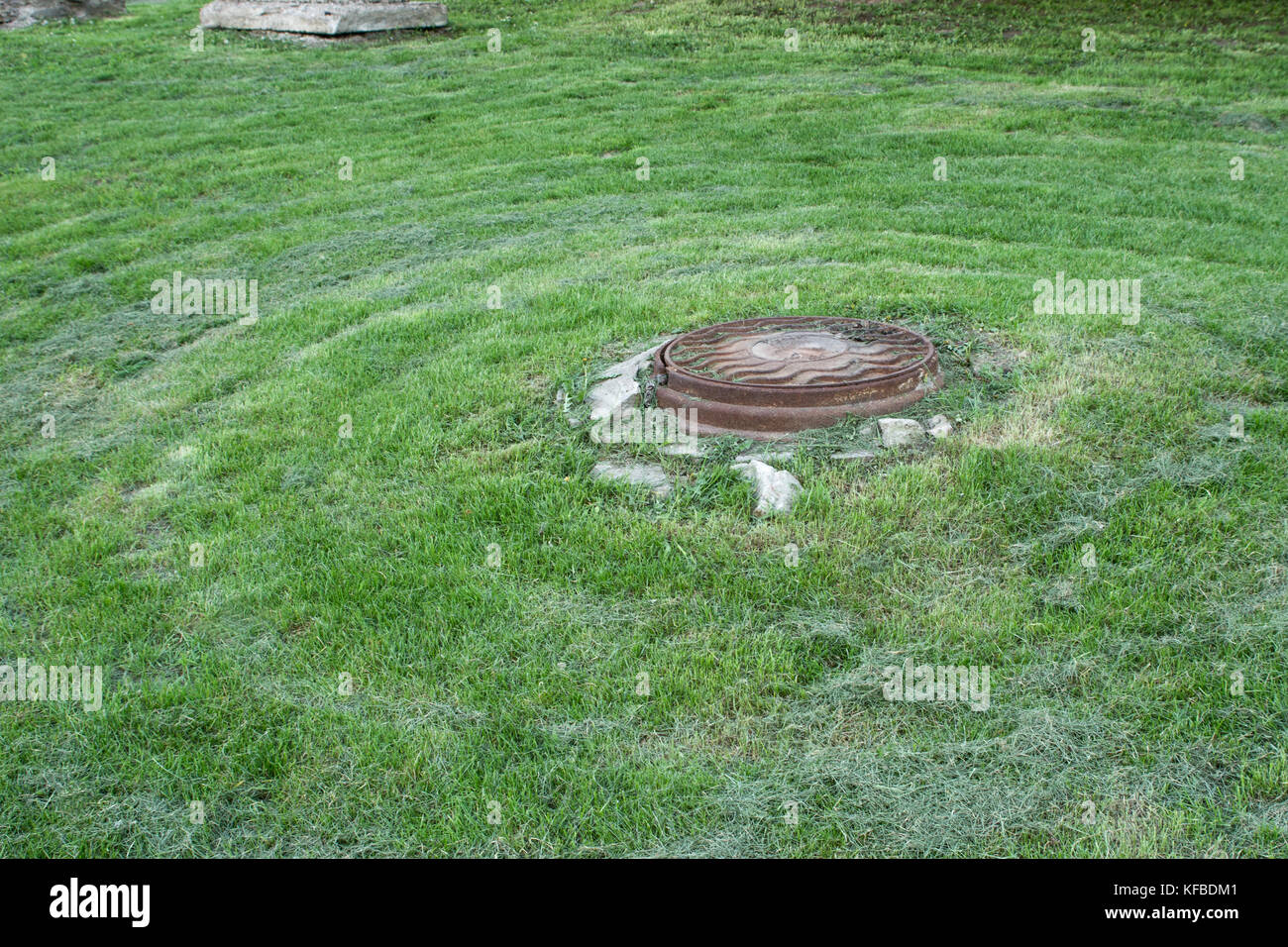 Rusty manhole on the lawn mowed in circles Stock Photo