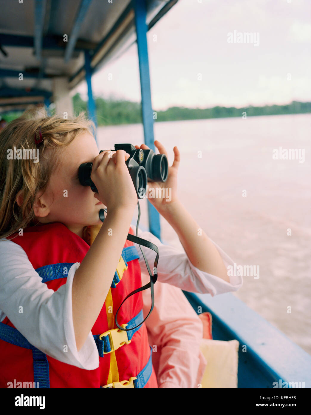 PERU, Amazon Rainforest, South America, Latin America, girl looking through binocular while travelling in boat along the Tambopata River. Stock Photo