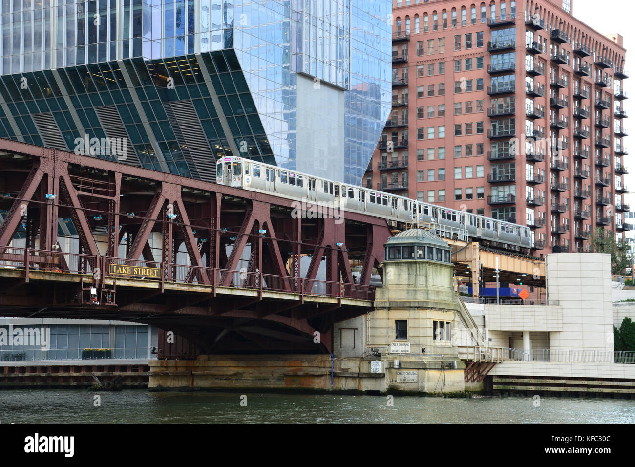 A pink line L train crosses the Chicago River at Lake Street in front of the cantilevered skyscraper at 150 N Riverside in Chicago Stock Photo