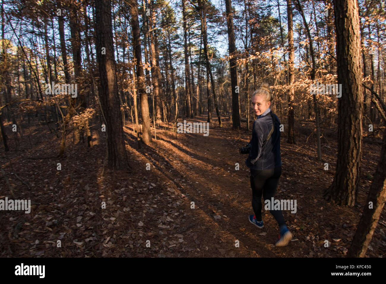 A blonde woman hiking in the autumn forest as the sun sets. In Georgia. Stock Photo