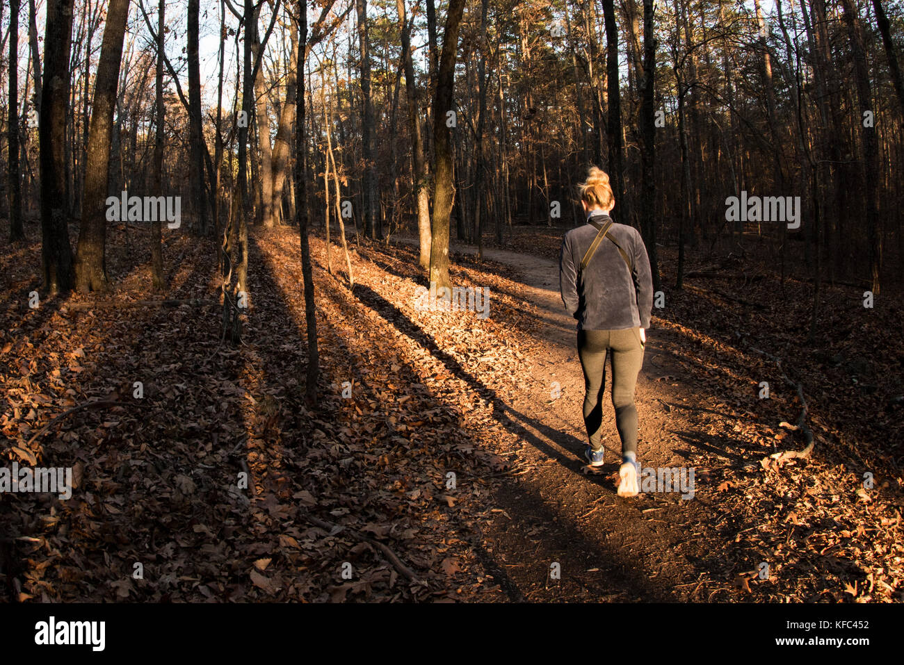 A blonde woman hiking in the autumn forest as the sun sets. In Georgia. Stock Photo